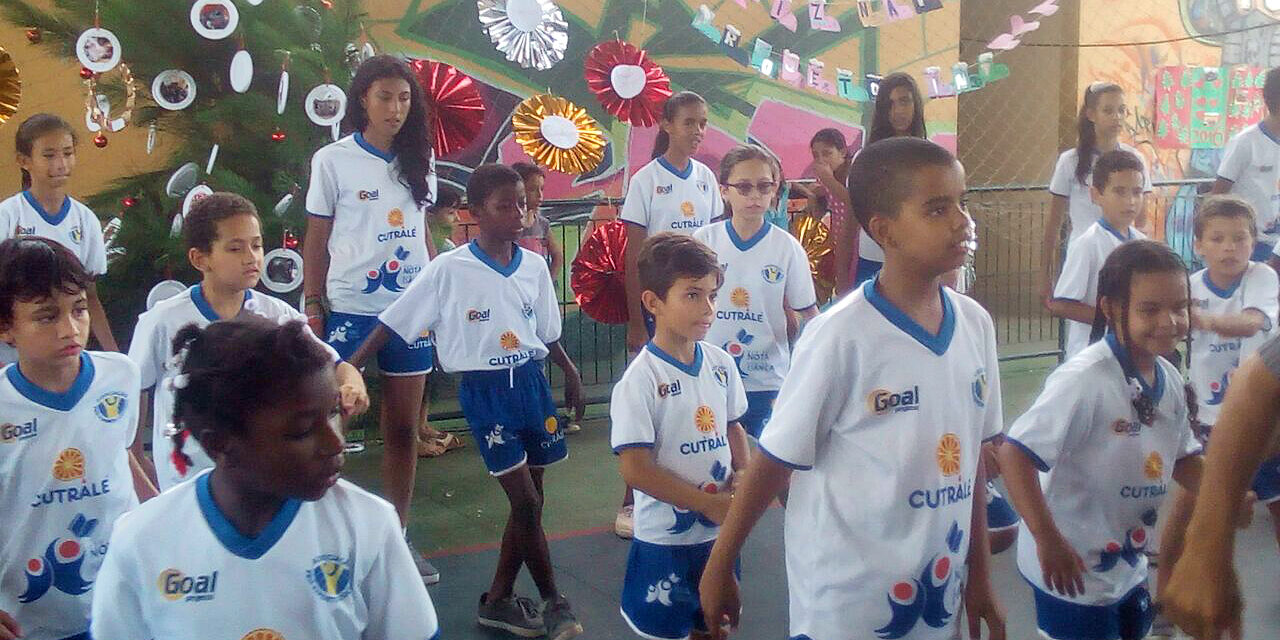 Crianças em uniformes se reúnem em quadra decorada para evento. Grupo de crianças e adolescentes com uniformes brancos e azuis em uma quadra decorada para evento.