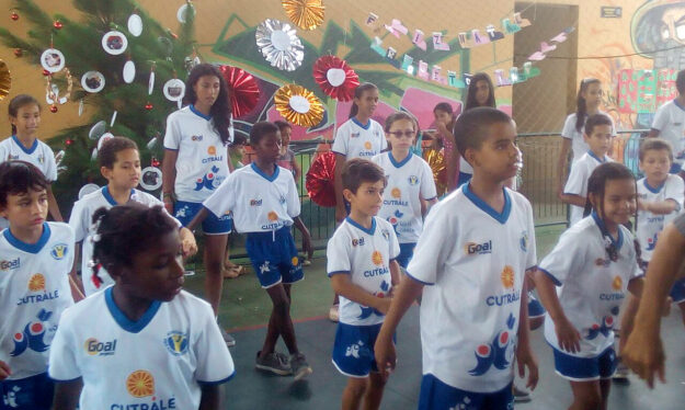 Crianças em uniformes se reúnem em quadra decorada para evento. Grupo de crianças e adolescentes com uniformes brancos e azuis em uma quadra decorada para evento.