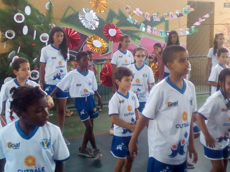 Crianças em uniformes se reúnem em quadra decorada para evento. Grupo de crianças e adolescentes com uniformes brancos e azuis em uma quadra decorada para evento.