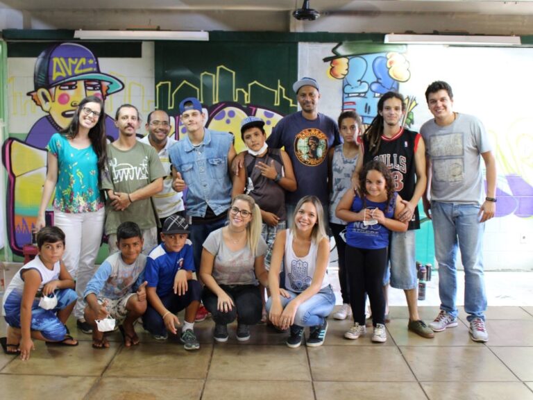 Encontro de grupo em sala com arte urbana. Grupo de adultos e crianças posa para foto em frente a uma parede de escola com grafite.