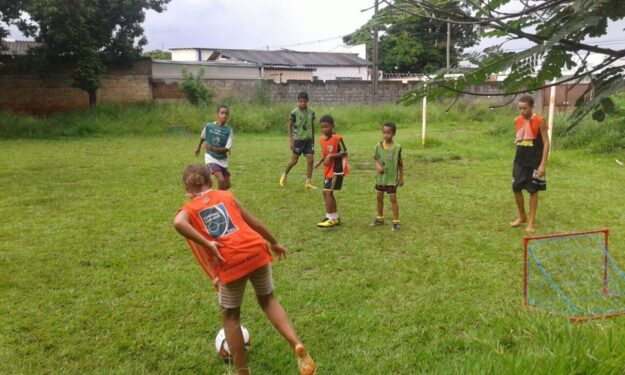 Crianças jogando futebol em campo gramado. Crianças jogando futebol em um campo gramado com uma pequena trave vermelha e azul em primeiro plano.