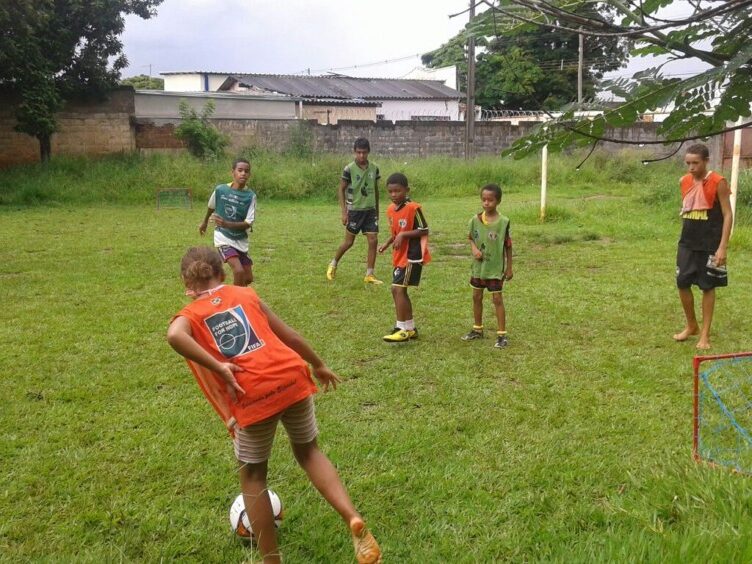 Crianças jogando futebol em campo gramado. Crianças jogando futebol em um campo gramado com uma pequena trave vermelha e azul em primeiro plano.