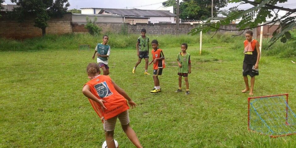 Crianças jogando futebol em campo gramado. Crianças jogando futebol em um campo gramado com uma pequena trave vermelha e azul em primeiro plano.