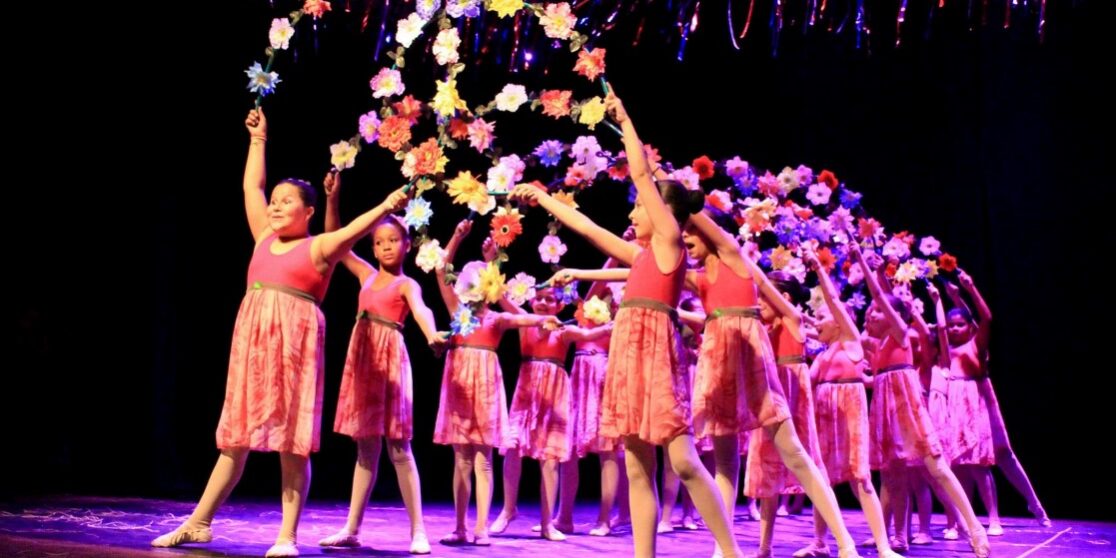 Coreografia floral: apresentação de balé infantil com guirlanda de flores. Dançarinas infantis em vestidos rosa com as mãos erguidas seguram uma guirlanda de flores em uma performance no palco.