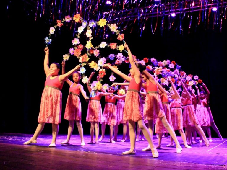 Coreografia floral: apresentação de balé infantil com guirlanda de flores. Dançarinas infantis em vestidos rosa com as mãos erguidas seguram uma guirlanda de flores em uma performance no palco.