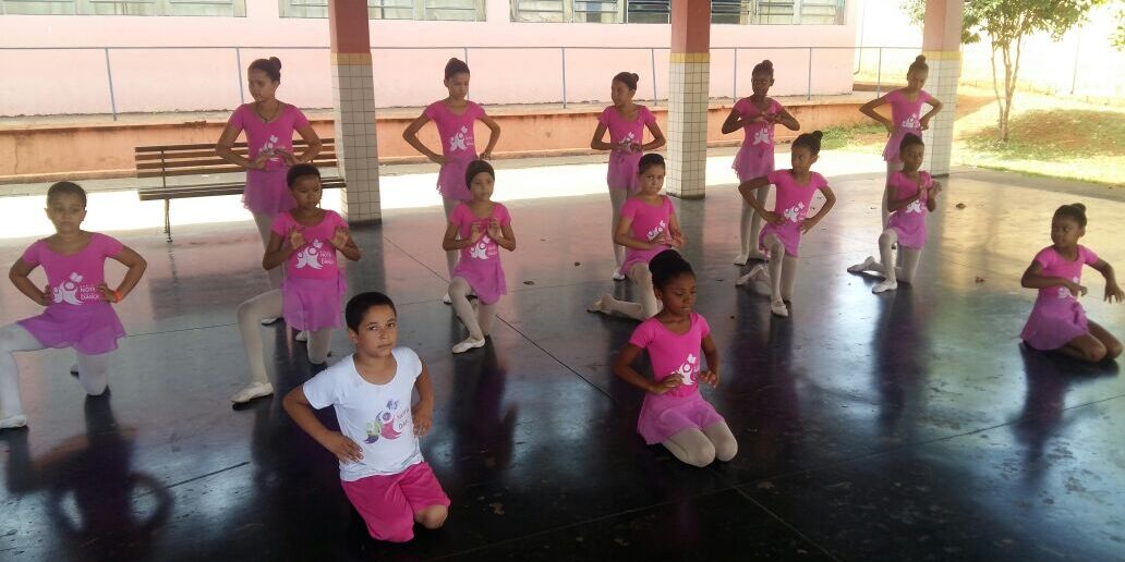 Coreografia de balé infantil em grupo com figurino rosa. Grupo de meninas, a maioria em trajes de balé cor de rosa, em diferentes poses e níveis em uma quadra externa coberta.