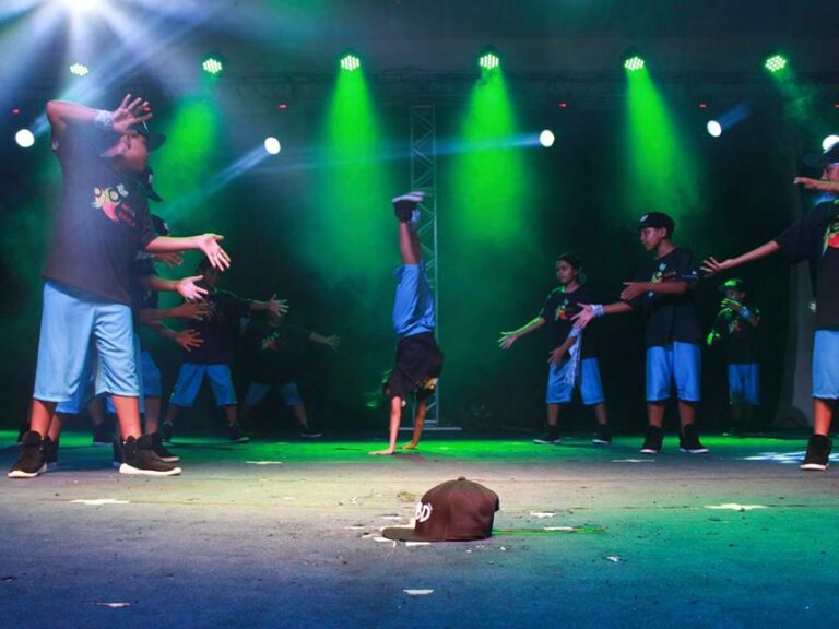 Performance de jovens no palco. Grupo de jovens se apresenta no palco com um dançarino de breakdance fazendo um headstand sob luzes verdes.