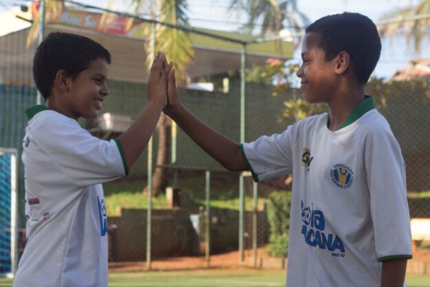 Amizade e espírito de equipe no projeto esportivo. Jovens participantes de projeto social esportivo celebram com um high-five, mostrando espírito de equipe.