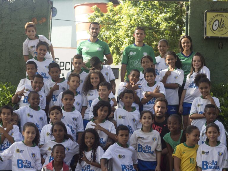 Equipe de futebol e alunos. Grande grupo de crianças e adultos em uniformes de futebol, posando para foto em escadaria externa com folhagens.