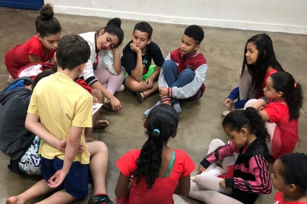 Roda de conversa e interação entre crianças. Grupo de crianças sentados em círculo no chão de uma sala, participando de uma roda de conversa.