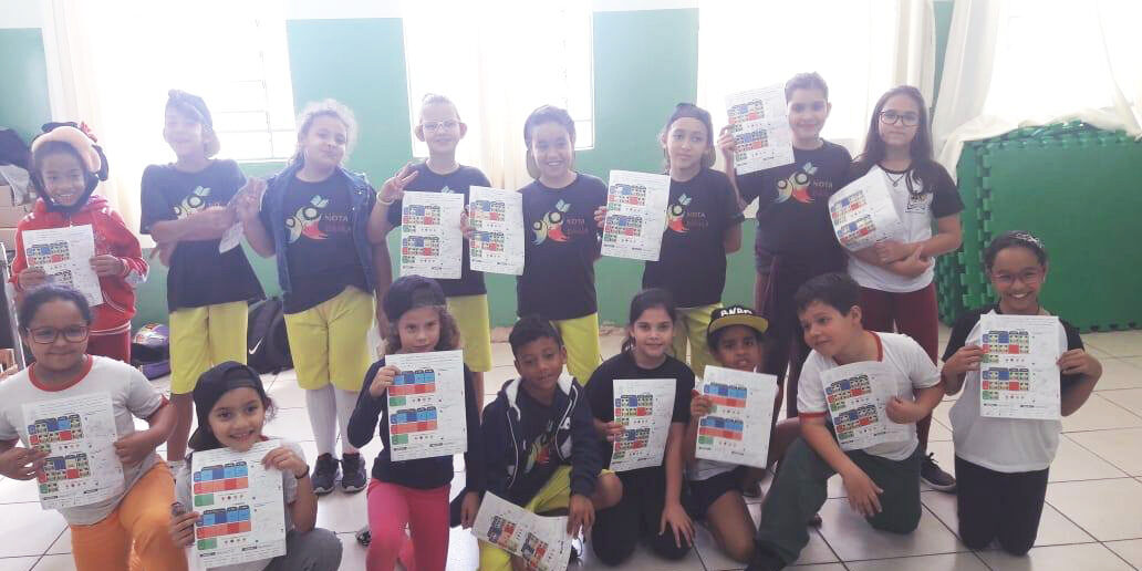 Conquista e sucesso em projetos infantis. Grupo de quatorze crianças em sala de aula, exibindo cartazes coloridos, sorrindo para a câmera.