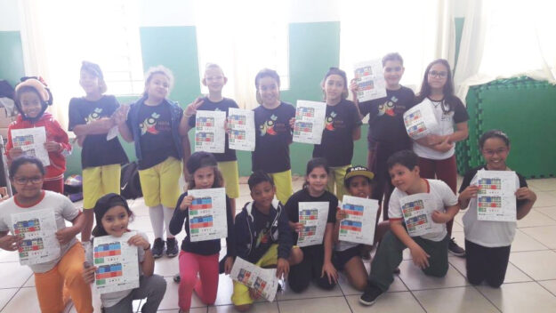 Grupo de quatorze crianças em sala de aula, exibindo cartazes coloridos, sorrindo para a câmera.