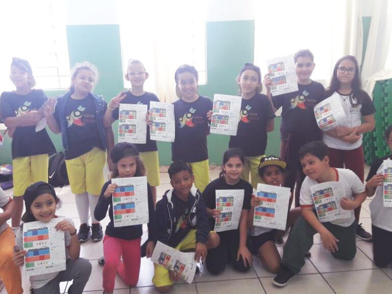 Conquista e sucesso em projetos infantis. Grupo de quatorze crianças em sala de aula, exibindo cartazes coloridos, sorrindo para a câmera.