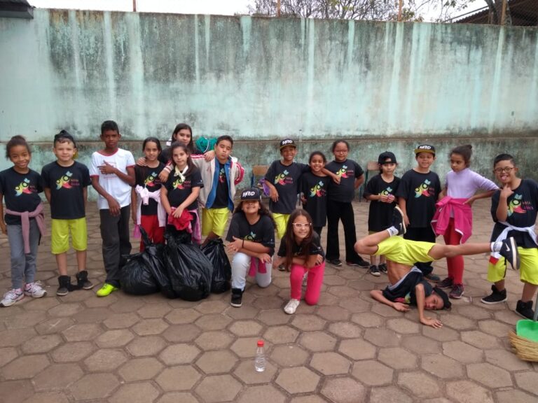 O Futuro em Ação: Crianças promovem a limpeza urbana. Grupo de crianças e jovens posa em pátio, com um deles realizando um movimento acrobático e sacos de lixo preto ao lado.