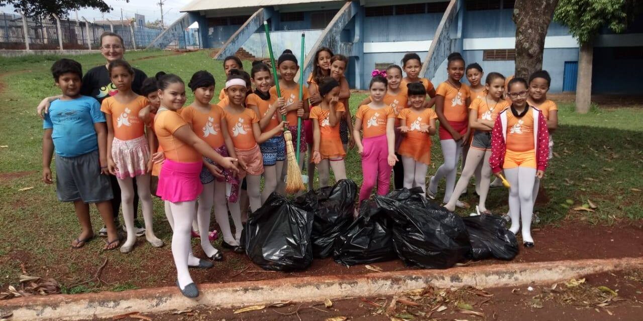 Cidadania em ação: alunos realizam Mutirão de Limpeza. Crianças e instrutor participam de mutirão de limpeza. Elas seguram vassouras e posam com sacos de lixo.