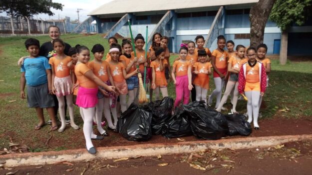 Cidadania em ação: alunos realizam Mutirão de Limpeza. Crianças e instrutor participam de mutirão de limpeza. Elas seguram vassouras e posam com sacos de lixo.