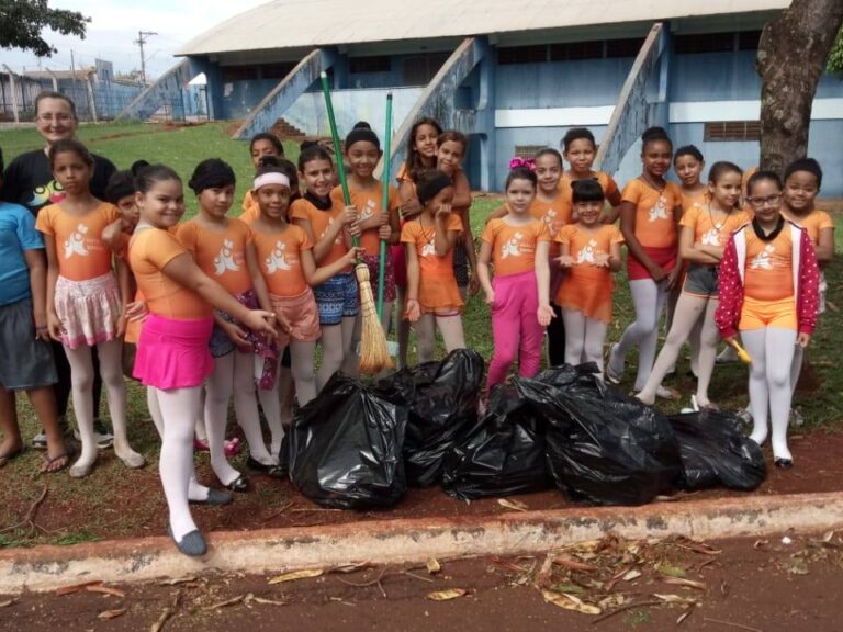 Cidadania em ação: alunos realizam Mutirão de Limpeza. Crianças e instrutor participam de mutirão de limpeza. Elas seguram vassouras e posam com sacos de lixo.