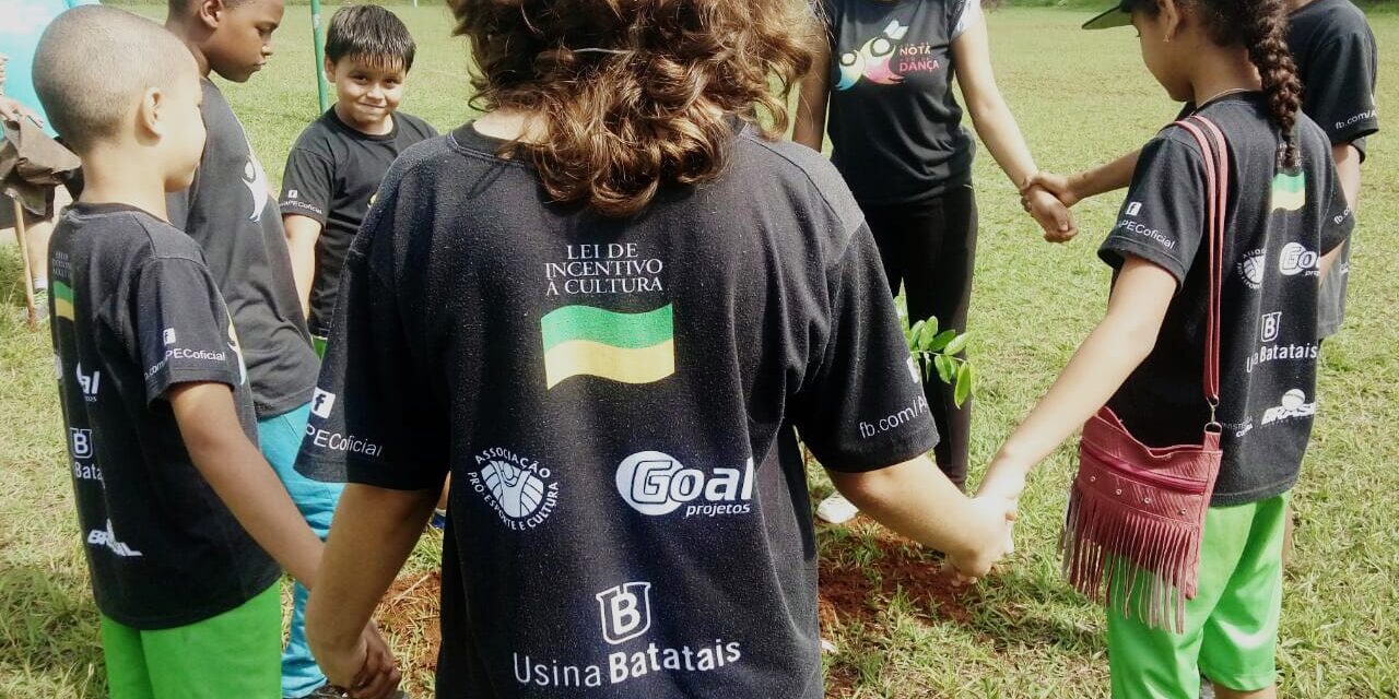 Crianças em Círculo e Lei de Incentivo à Cultura Crianças em círculo, de mãos dadas, em campo gramado. Camiseta preta com "Lei de Incentivo à Cultura" em destaque.