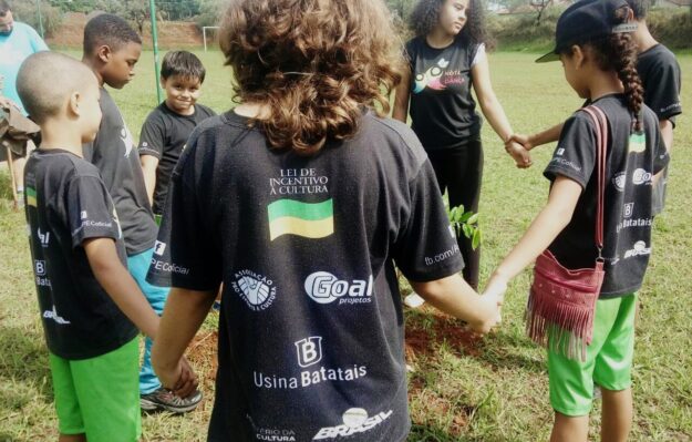 Crianças em Círculo e Lei de Incentivo à Cultura Crianças em círculo, de mãos dadas, em campo gramado. Camiseta preta com "Lei de Incentivo à Cultura" em destaque.