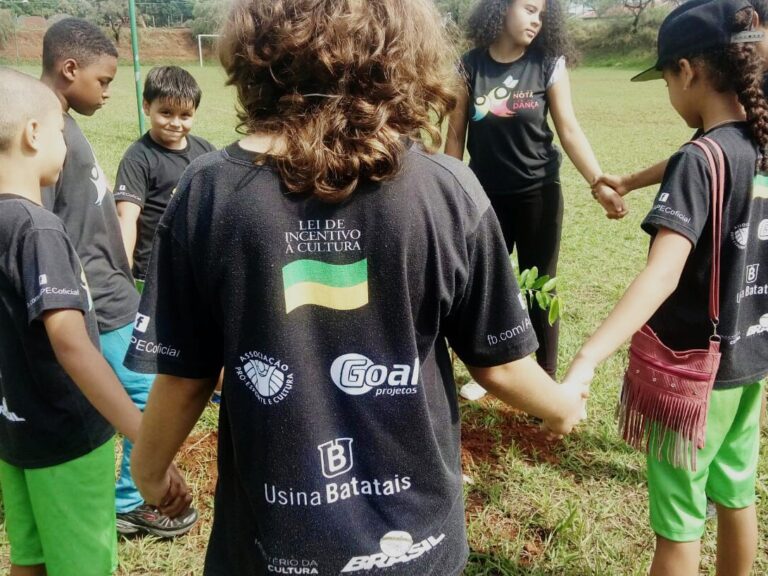 Crianças em Círculo e Lei de Incentivo à Cultura Crianças em círculo, de mãos dadas, em campo gramado. Camiseta preta com "Lei de Incentivo à Cultura" em destaque.
