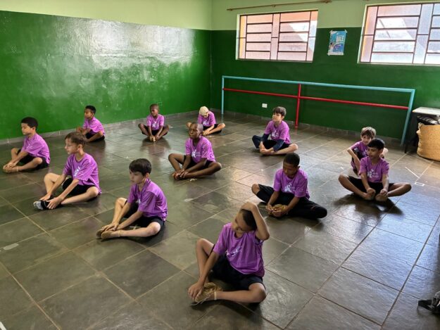 O balé também é deles Grupo de doze meninos em camisetas roxas sentados no chão de um estúdio de dança na aula de balé.