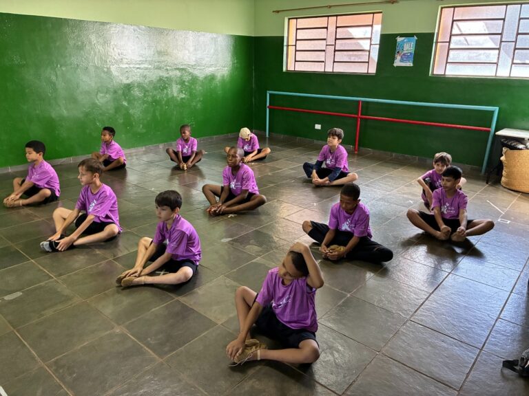 O balé também é deles Grupo de doze meninos em camisetas roxas sentados no chão de um estúdio de dança na aula de balé.